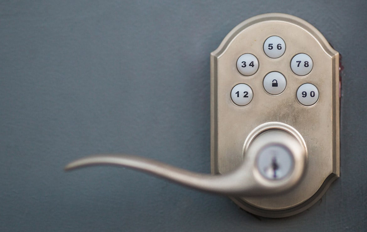 A close-up image of a keypad door lock with a silver-colored handle on a gray door. The keypad has buttons labeled with numbers from 1 to 9 and 0 in pairs (12, 34, 56, 78, 90). The keyhole is located underneath the handle. This security feature is part of our portfolio at Orand Capital.